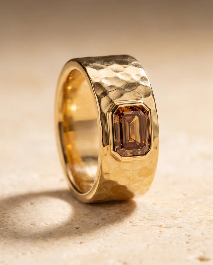 A wide 18k yellow gold band with a hand-hammered surface, flush-set with an emerald-cut cognac diamond