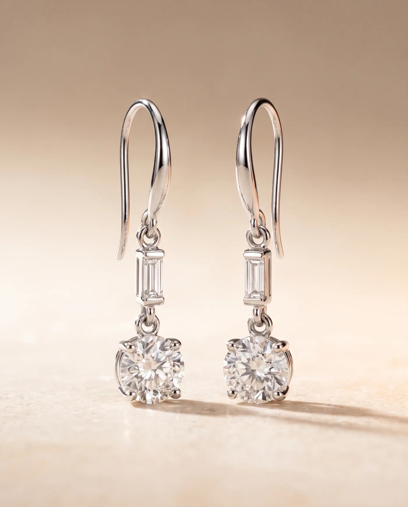 A pair of platinum drop earrings, each a baguette diamond suspended above a larger round brilliant on a shepherd hook
