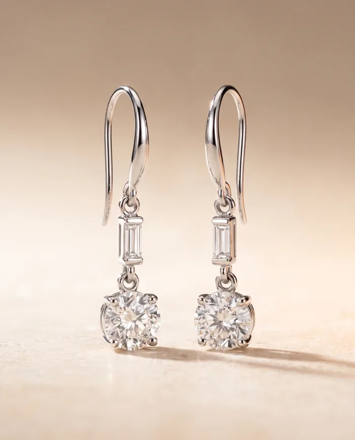 A pair of platinum drop earrings, each a baguette diamond suspended above a larger round brilliant on a shepherd hook