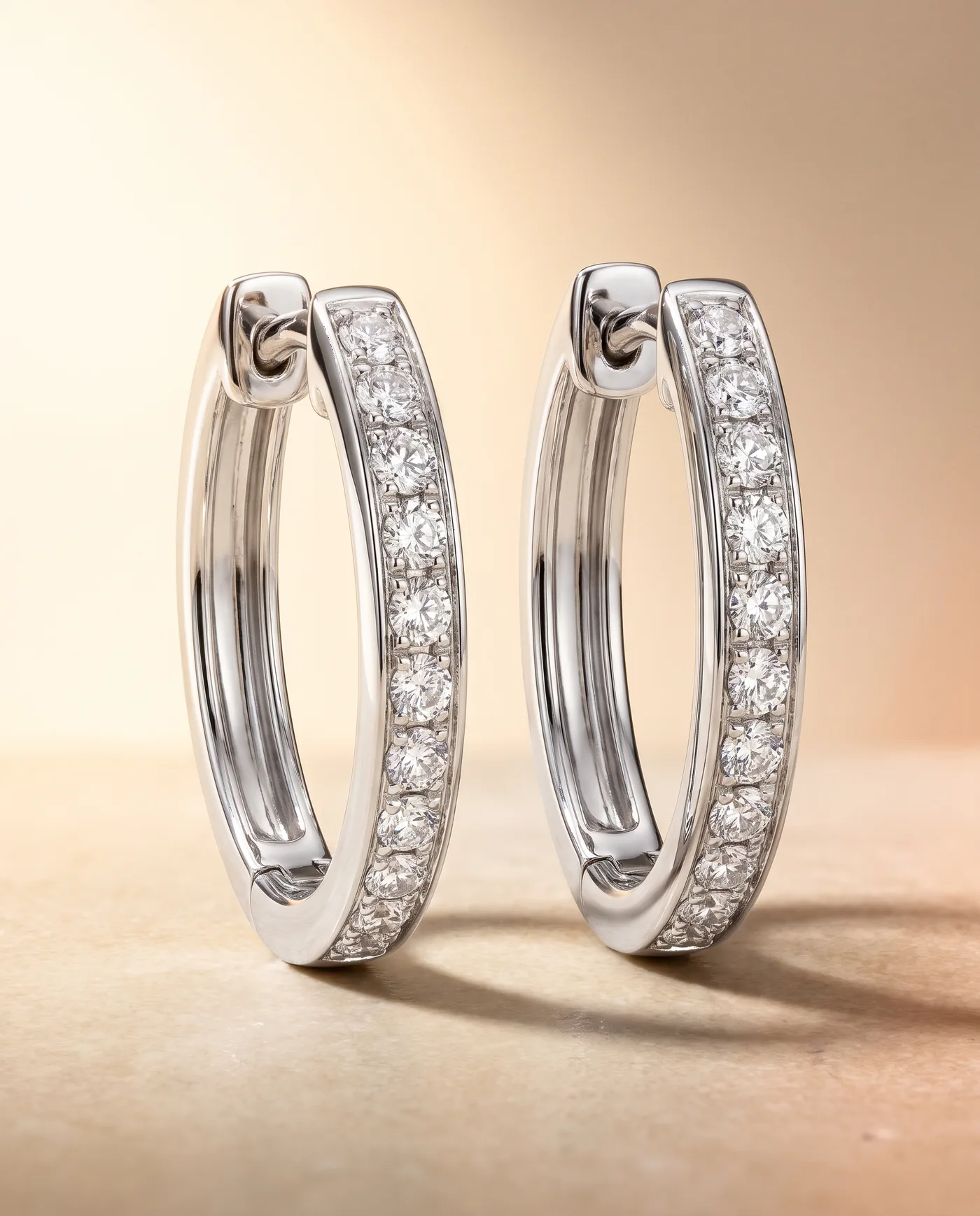 A pair of slim 18k white gold hoop earrings set with pavé round brilliant diamonds along the outer face